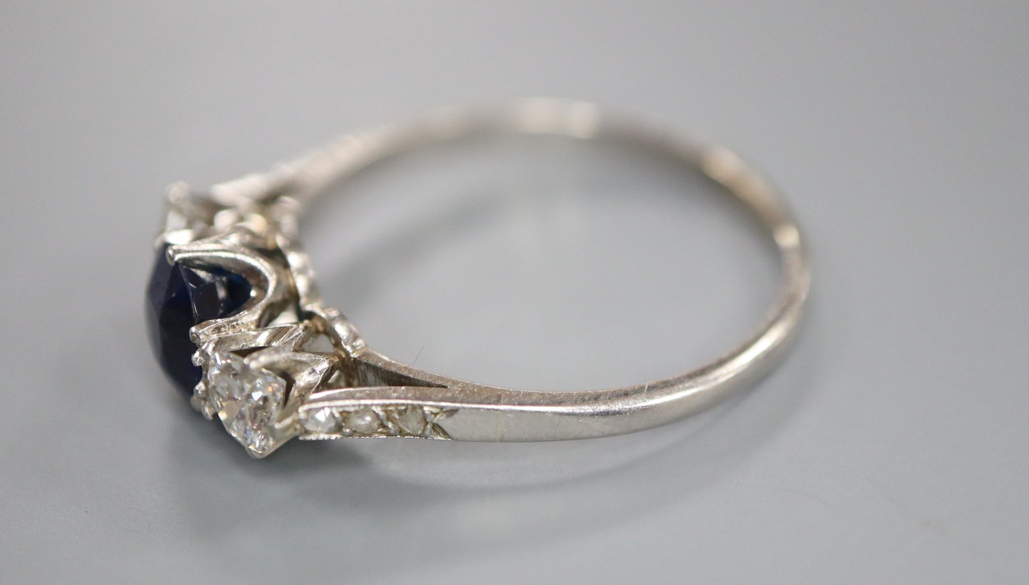 A white metal, sapphire and diamond three stone ring, with diamond chip set shoulders, size Q, gross 3.6 grams.